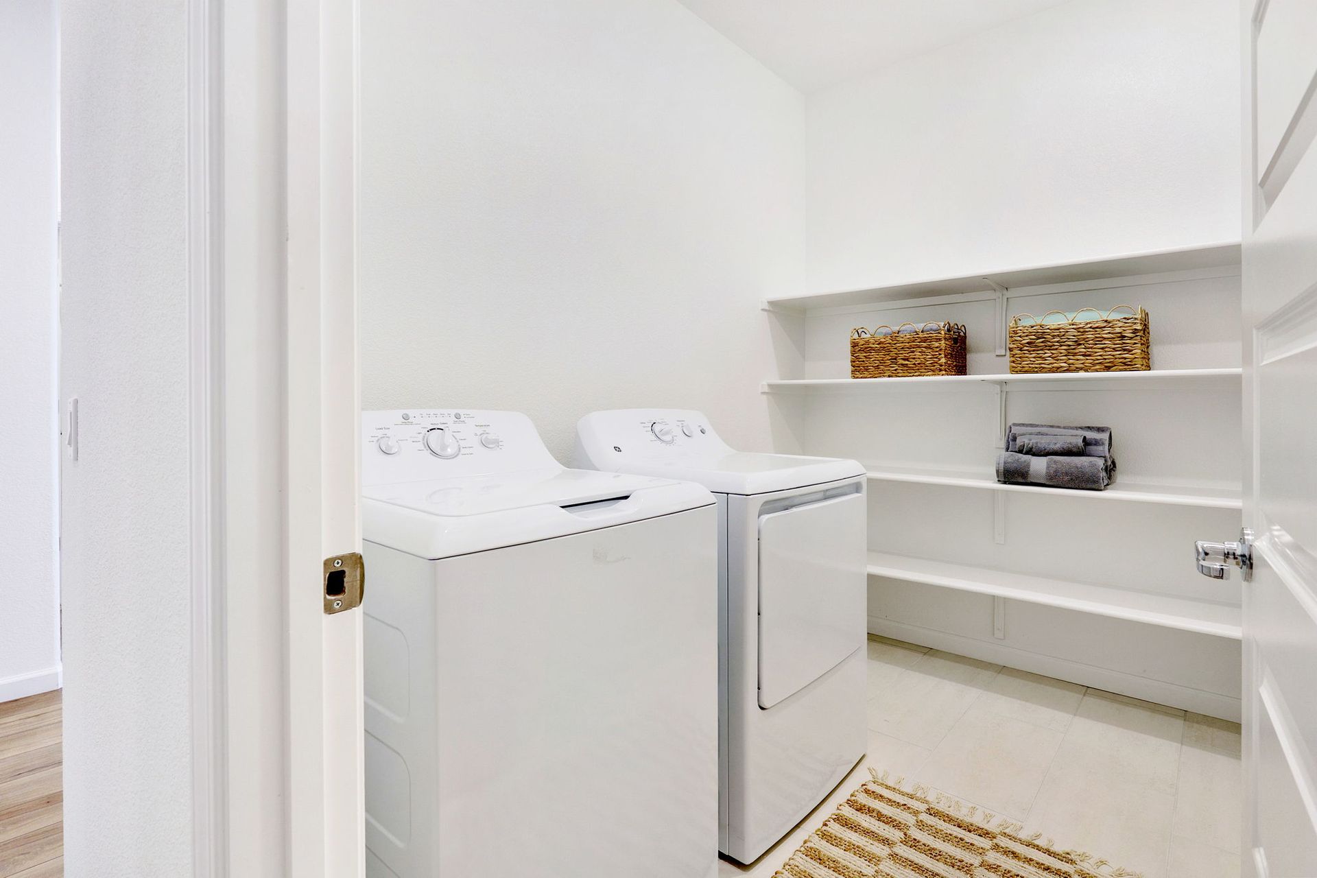 White laundry room with washer, dryer, and shelves holding baskets and towels.