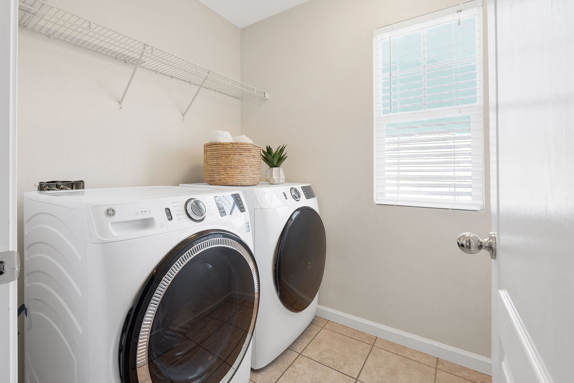 Laundry room with a washer and dryer, basket, and window with blinds.