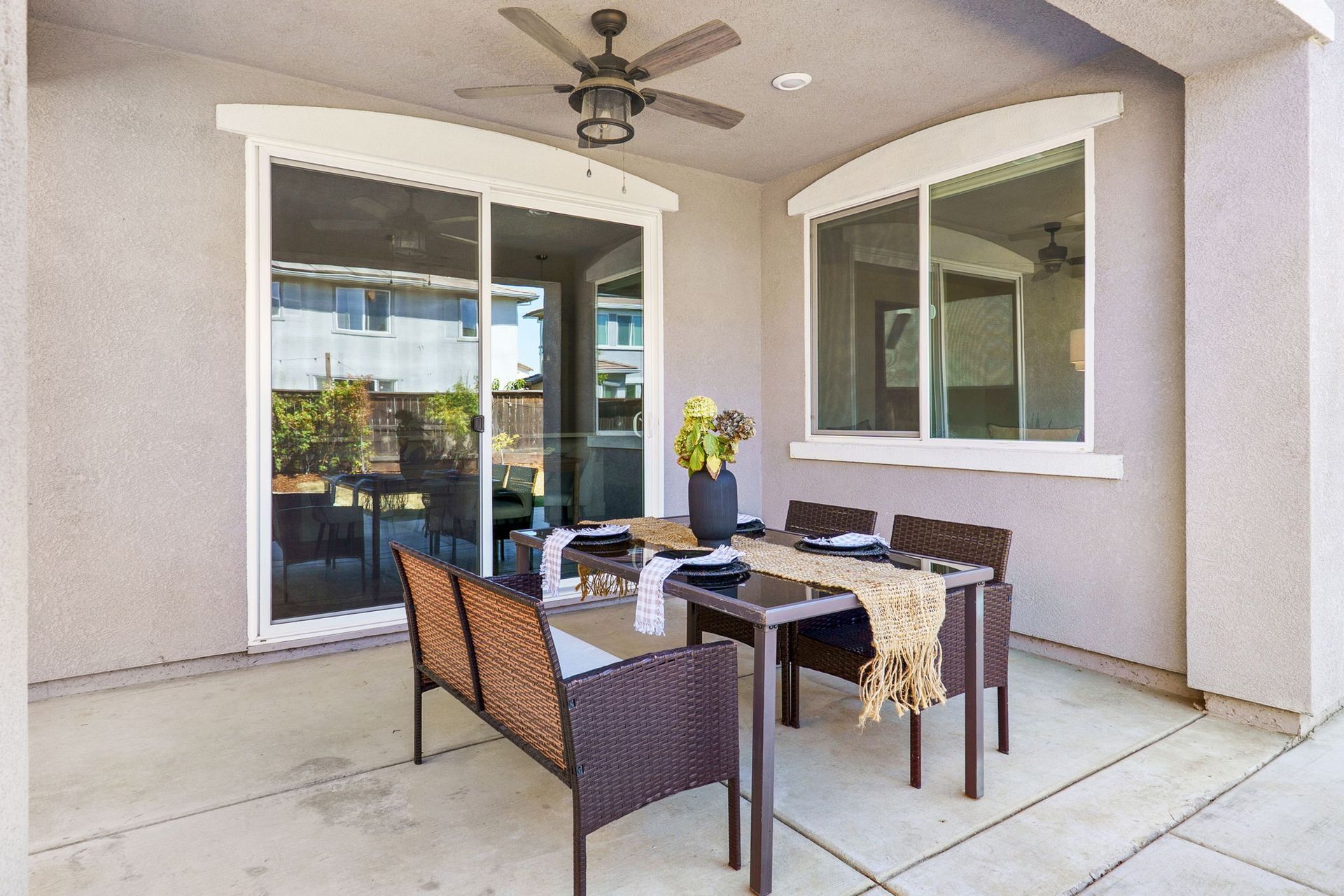 Patio with dining table set for four, wicker bench, and ceiling fan. Sliding glass door and window.