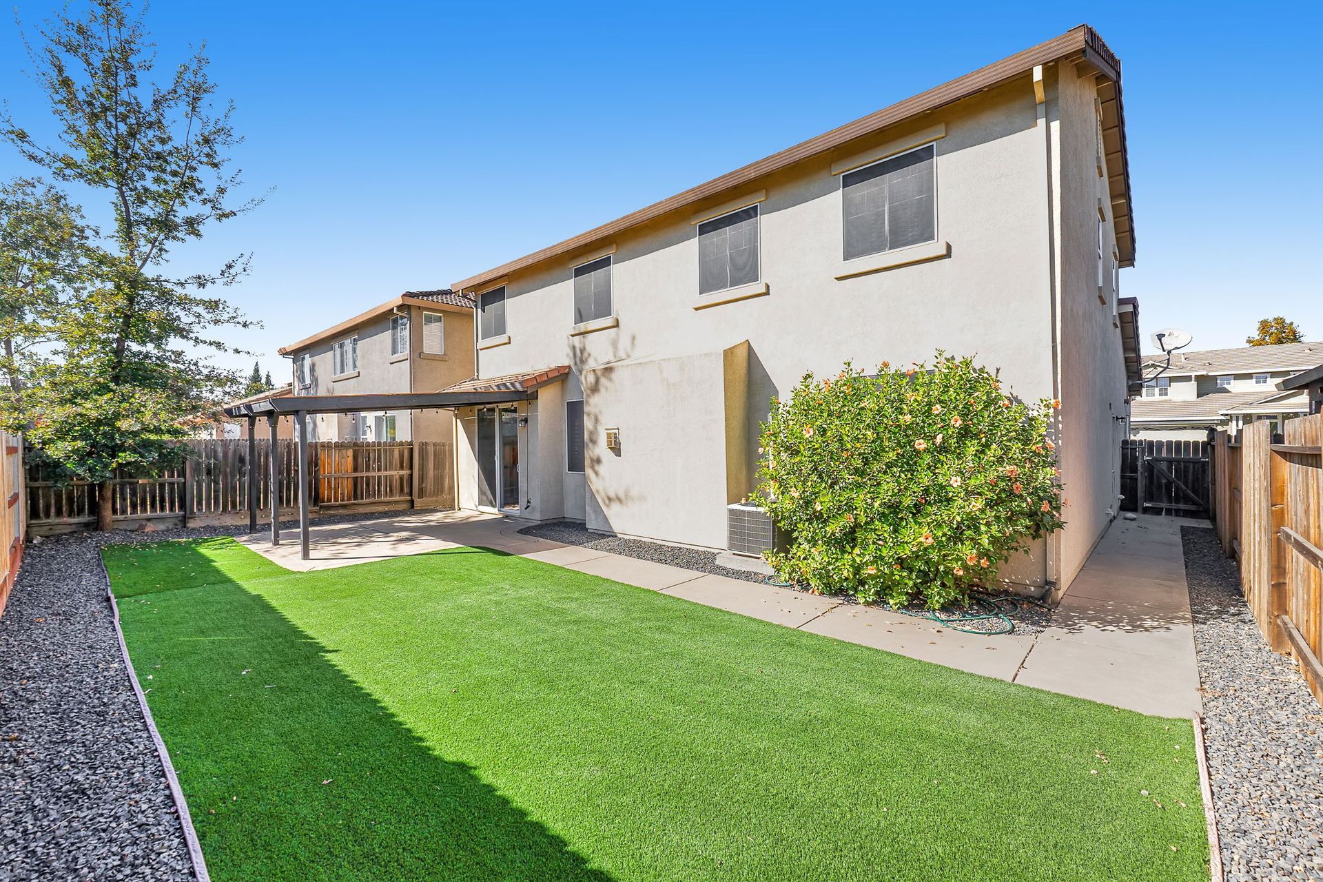Rear exterior of a tan townhome with a pergola over a patio and artificial turf lawn.