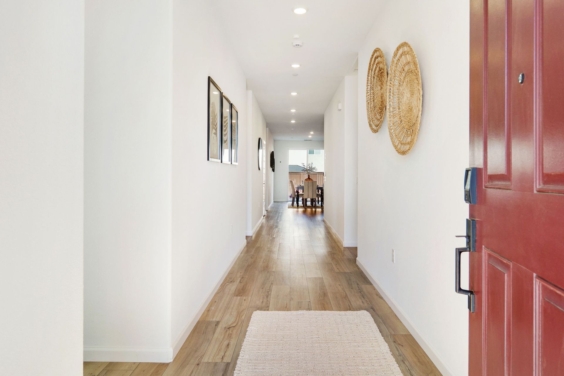 Narrow hallway with white walls, light wood floor, and a red door.