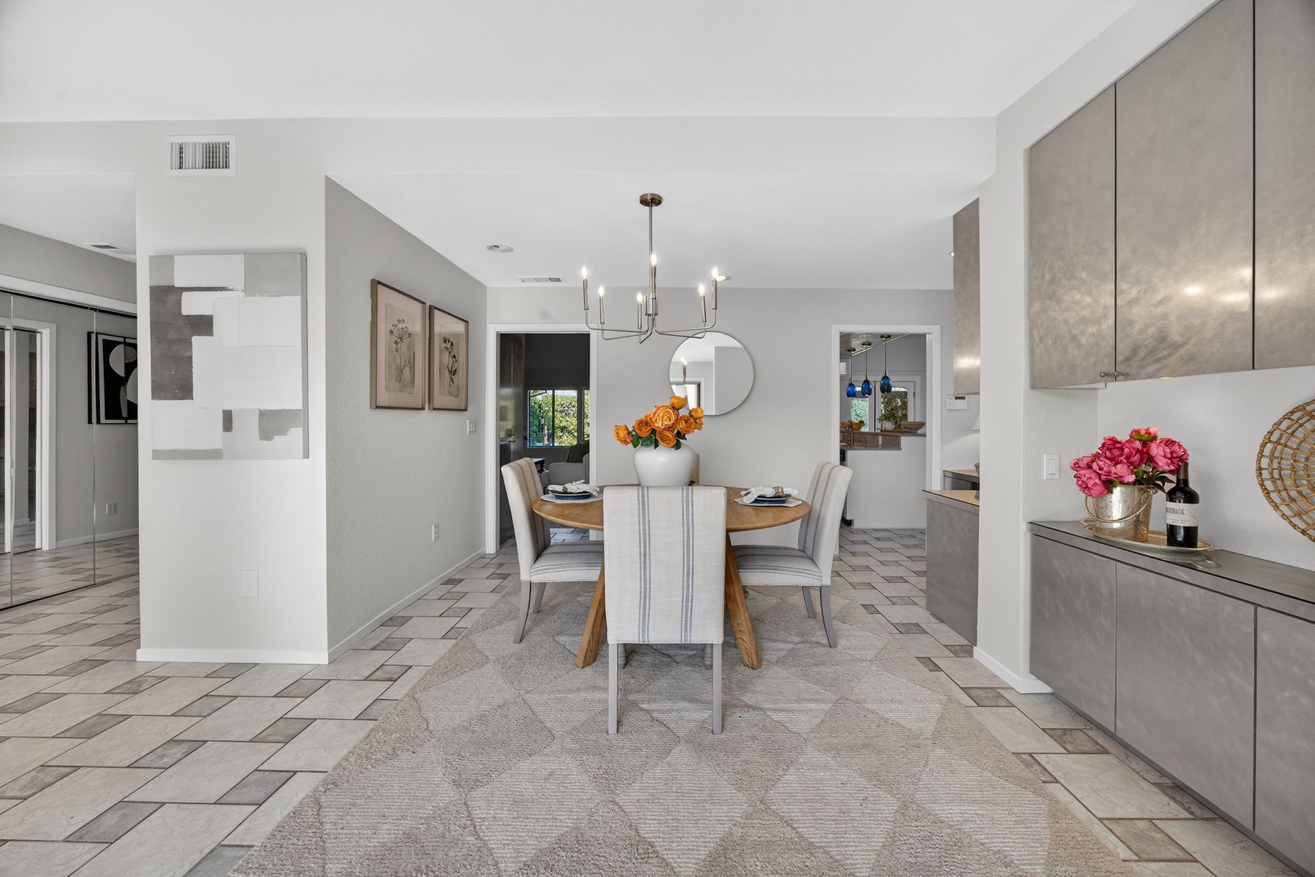 Dining room with table, chairs, flowers, rug, chandelier, and modern cabinetry.