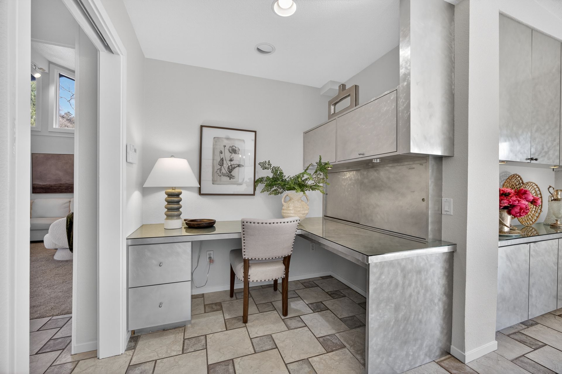 Built-in metal desk area in a home. Includes chair, artwork, lamp, and cabinet. Gray and neutral tones throughout.