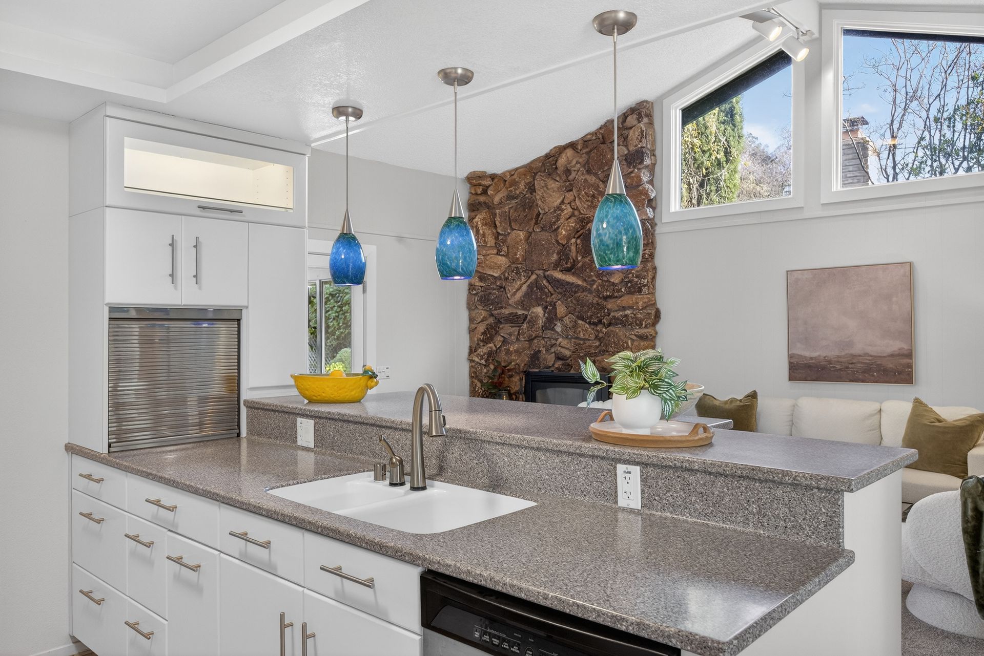 Kitchen with granite countertop, white cabinets, blue pendant lights, and a stone wall.