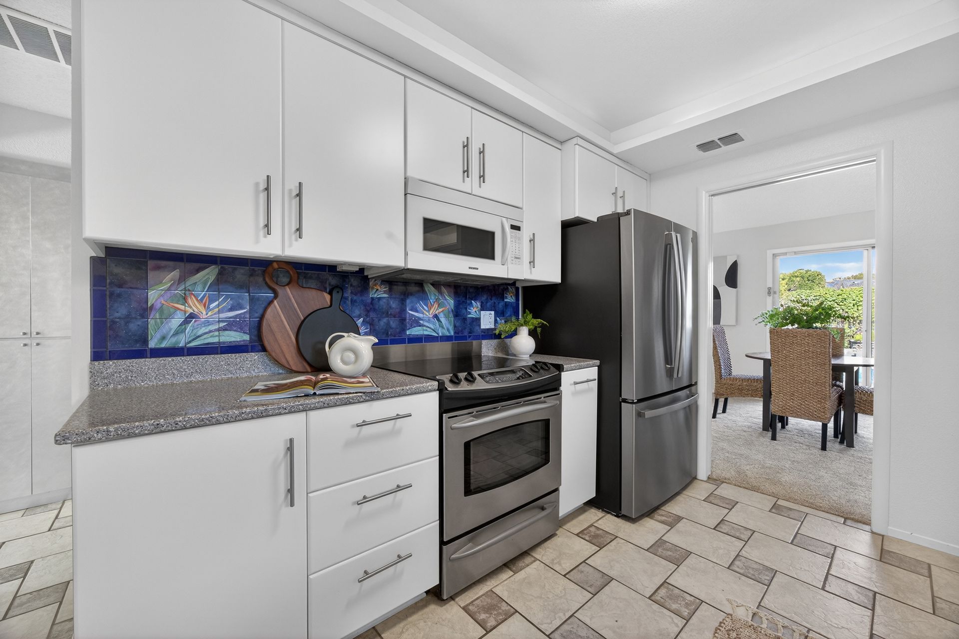 White kitchen with stainless steel appliances, blue tile backsplash, and a view into the dining area.
