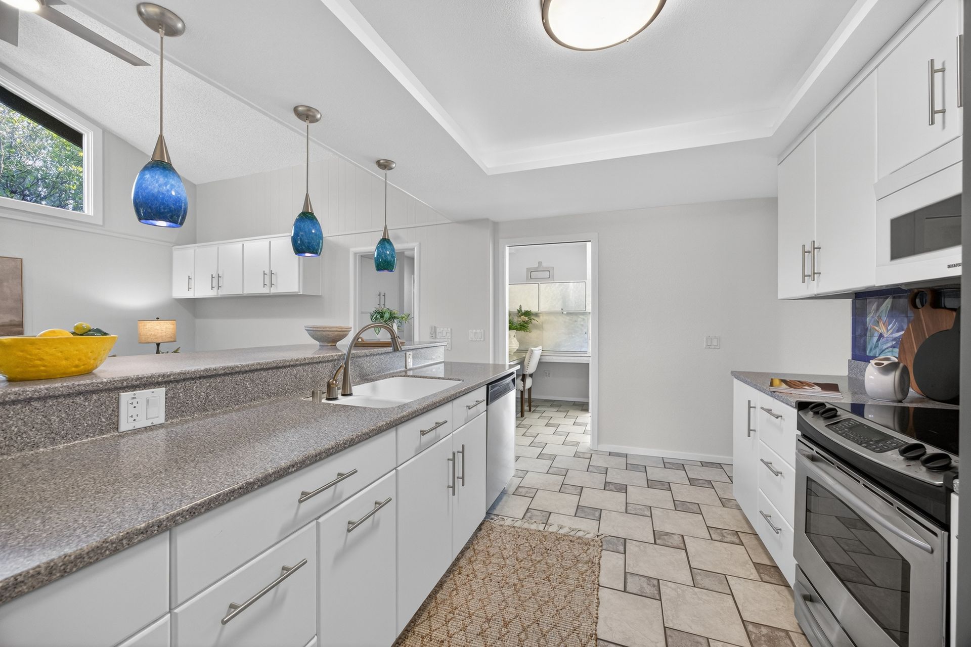 Bright white kitchen with gray countertops, blue pendant lights, and patterned tile floor.