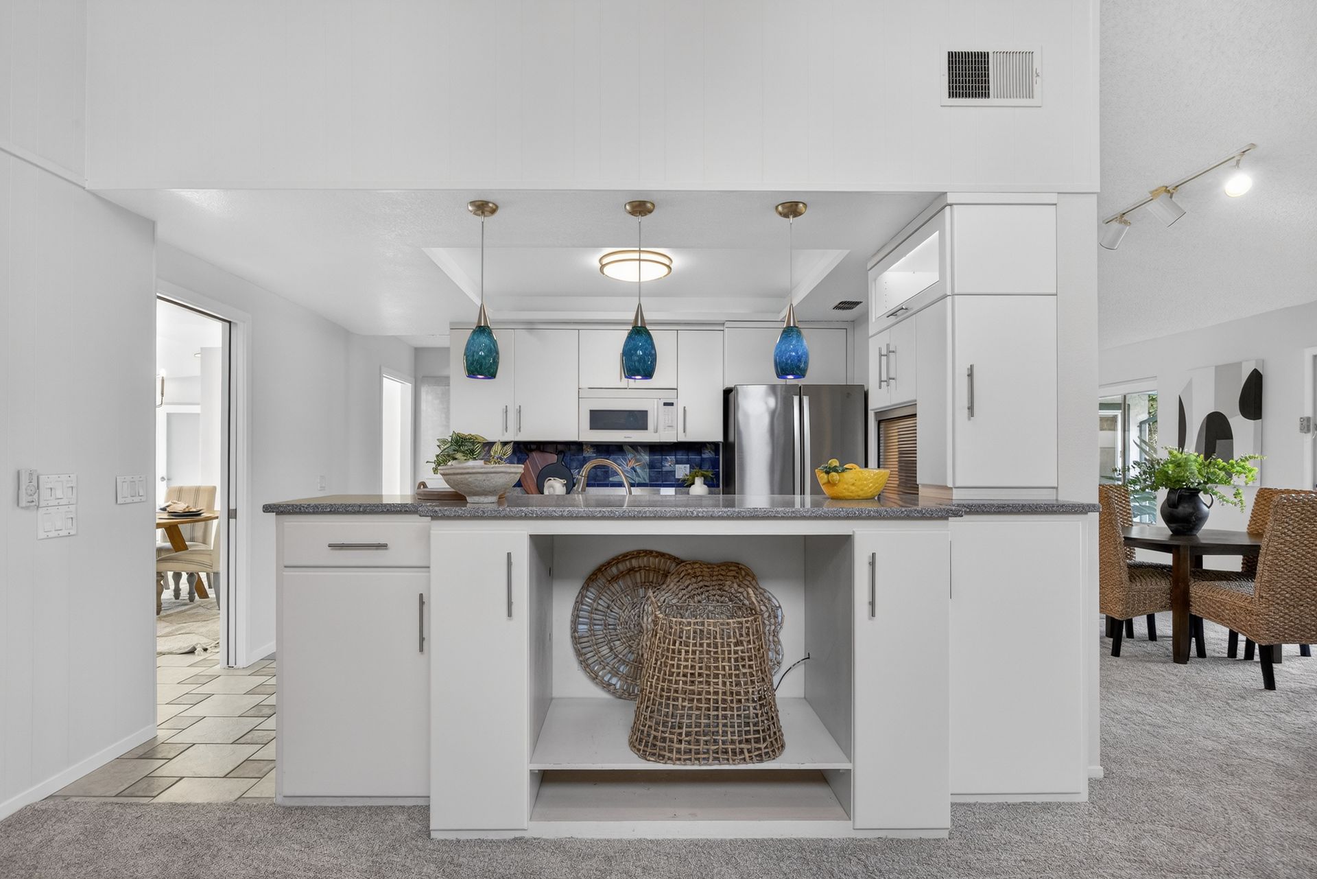 Open kitchen with white cabinets, gray countertops, and blue pendant lights.