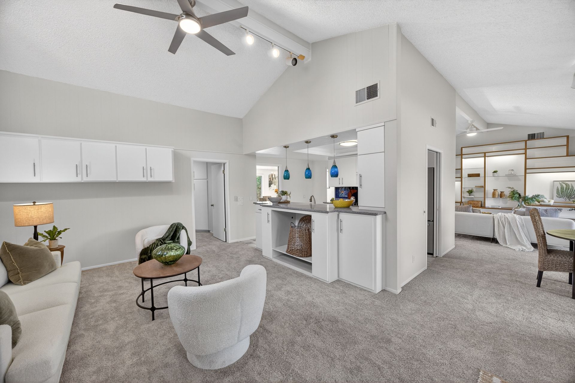 Living room with white walls, high ceiling, and light gray carpet. Furnished with white sofa, chairs, and a coffee table.