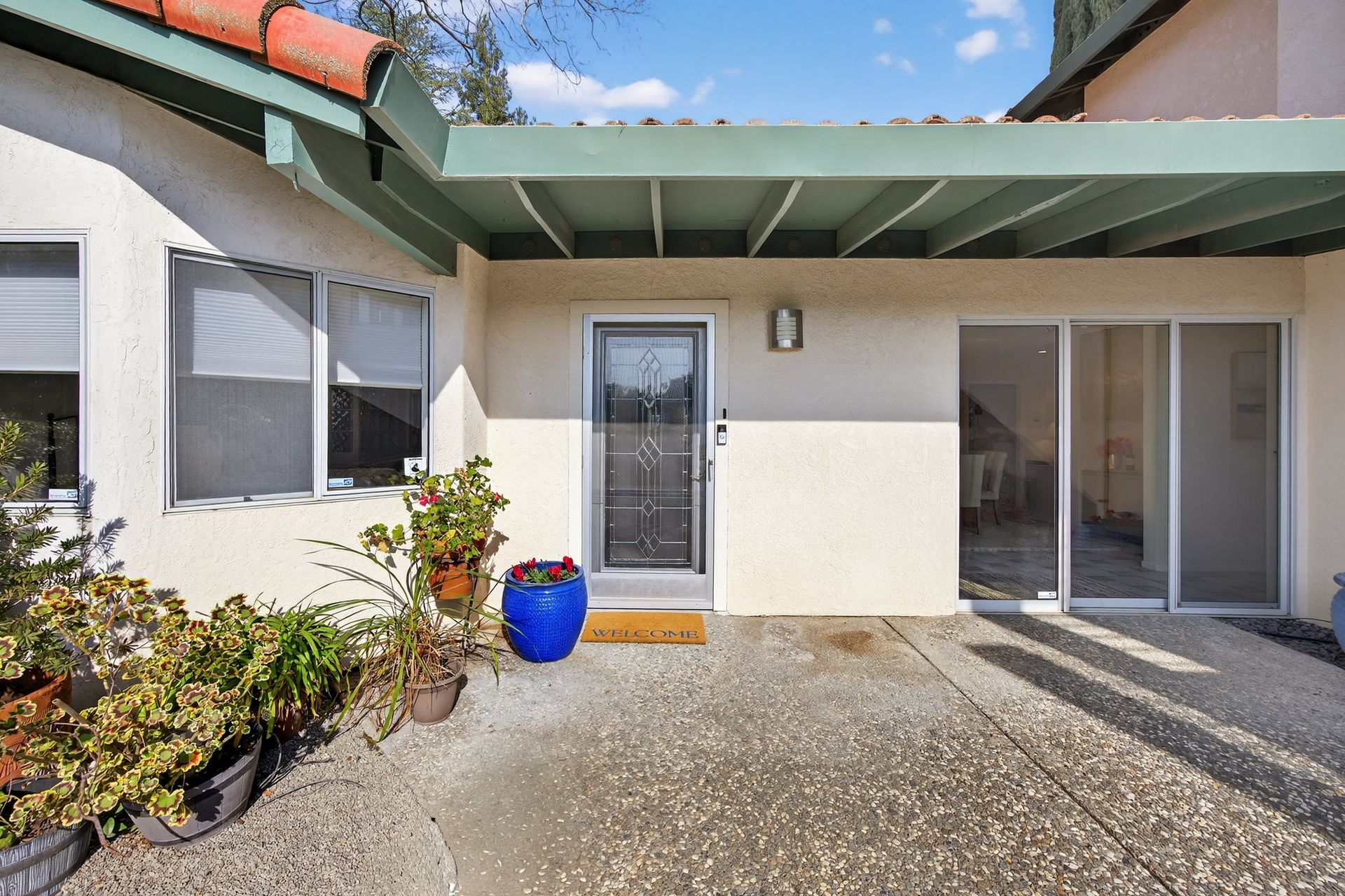 Exterior of a home with a door, sliding glass door, and a patio with potted plants.