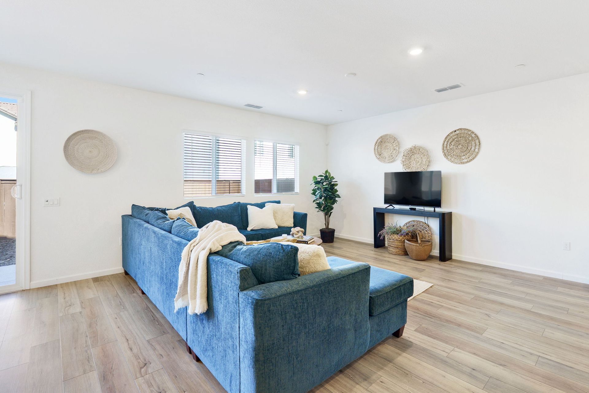 A modern living room with a blue sectional sofa, TV, and decorative wall art. Light wood floors and white walls.