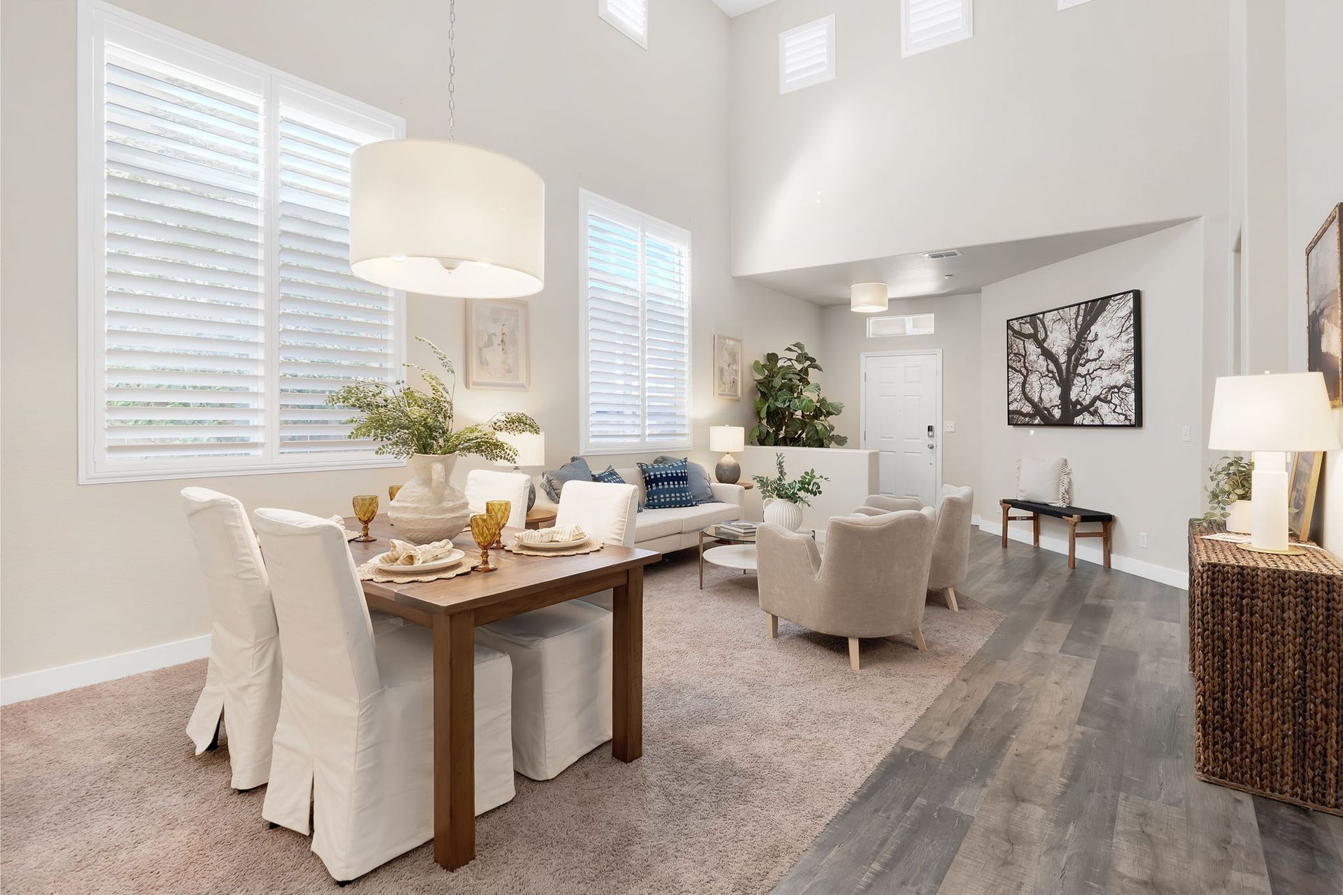 Dining room with table set for a meal, connected to a living area with sofas, chairs, and large windows.