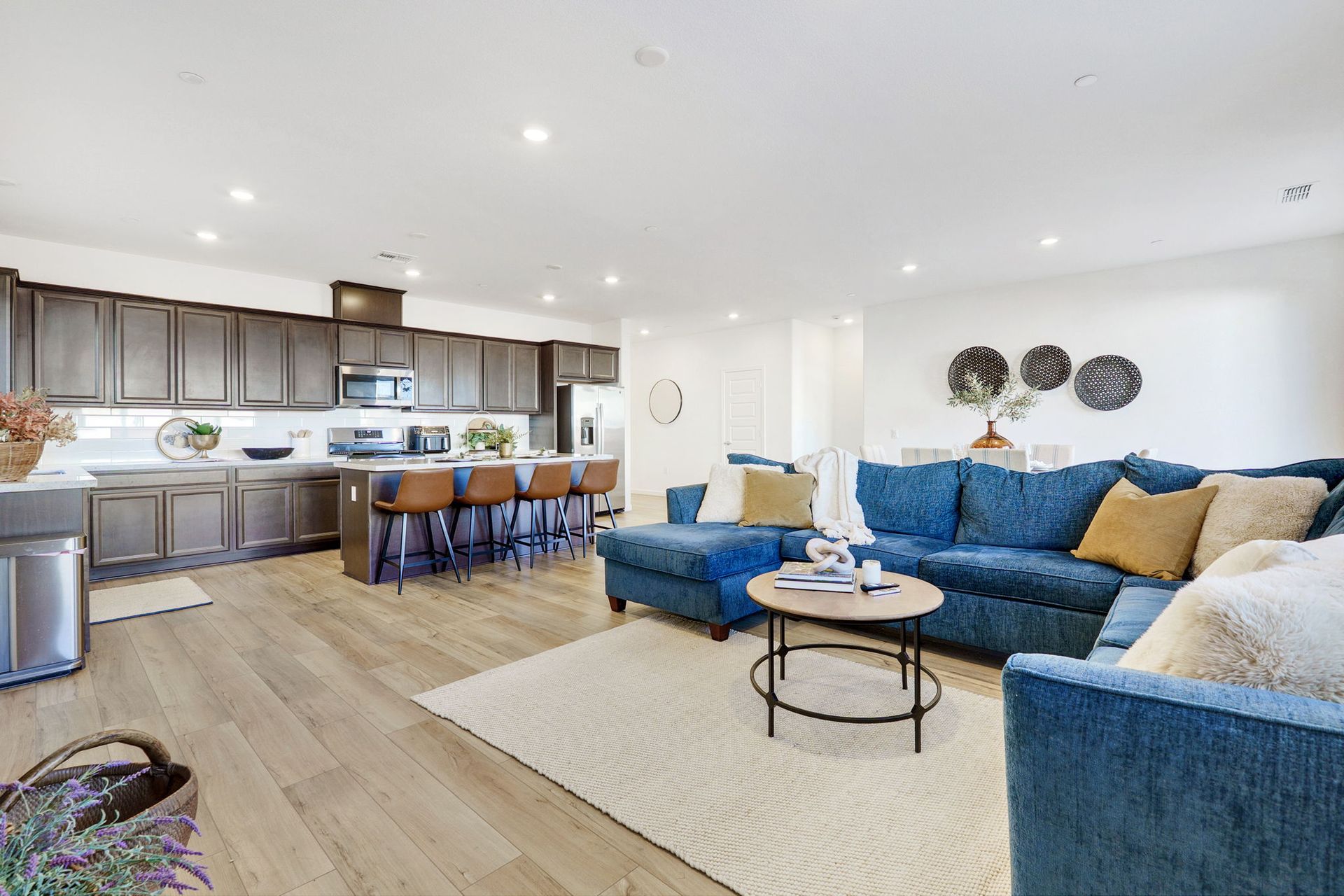 Open-concept kitchen and living room with blue sectional, light wood floors, and dark cabinets.