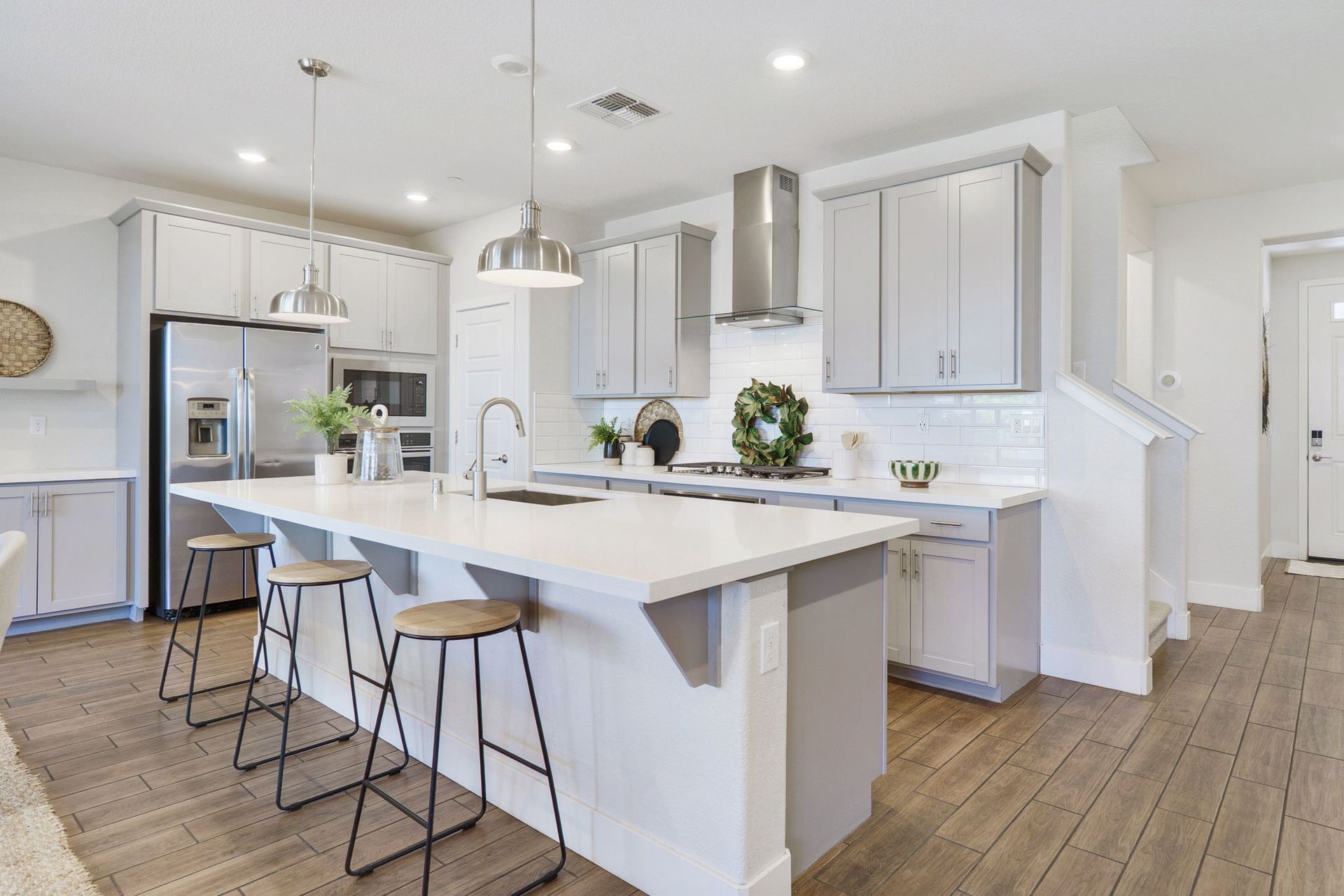 Modern kitchen with gray cabinets, white countertops, stainless steel appliances, and a central island with stools.