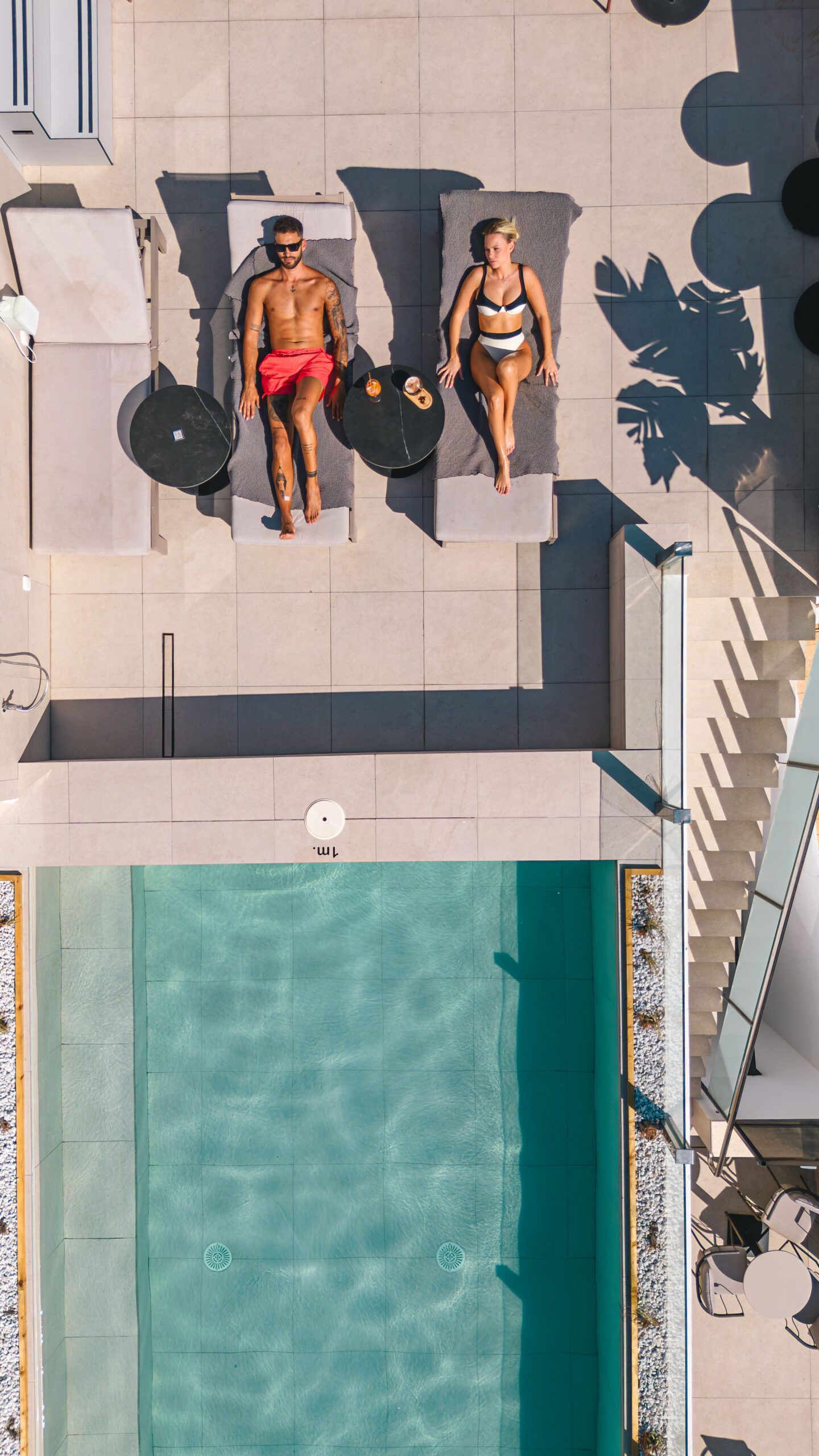 An aerial view of a man and a woman sitting on lounge chairs next to a swimming pool.