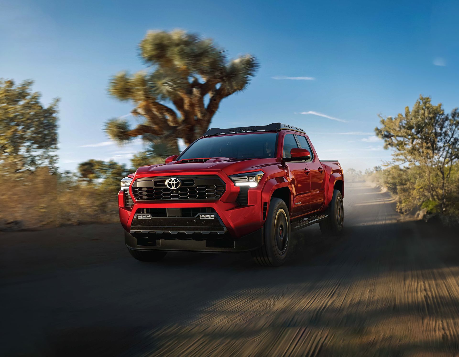 Un Toyota Tacoma rojo conduce por un camino de tierra.