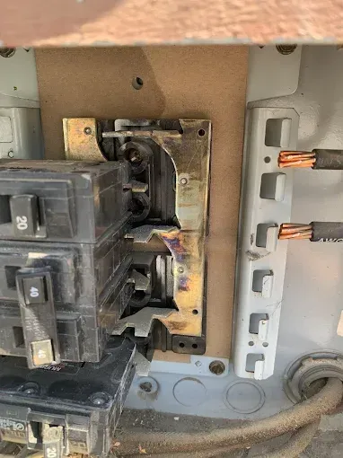 HVAC technician kneeling, inspecting a furnace. Wearing blue shirt, ball cap, and protective shoe covers. Interior setting.