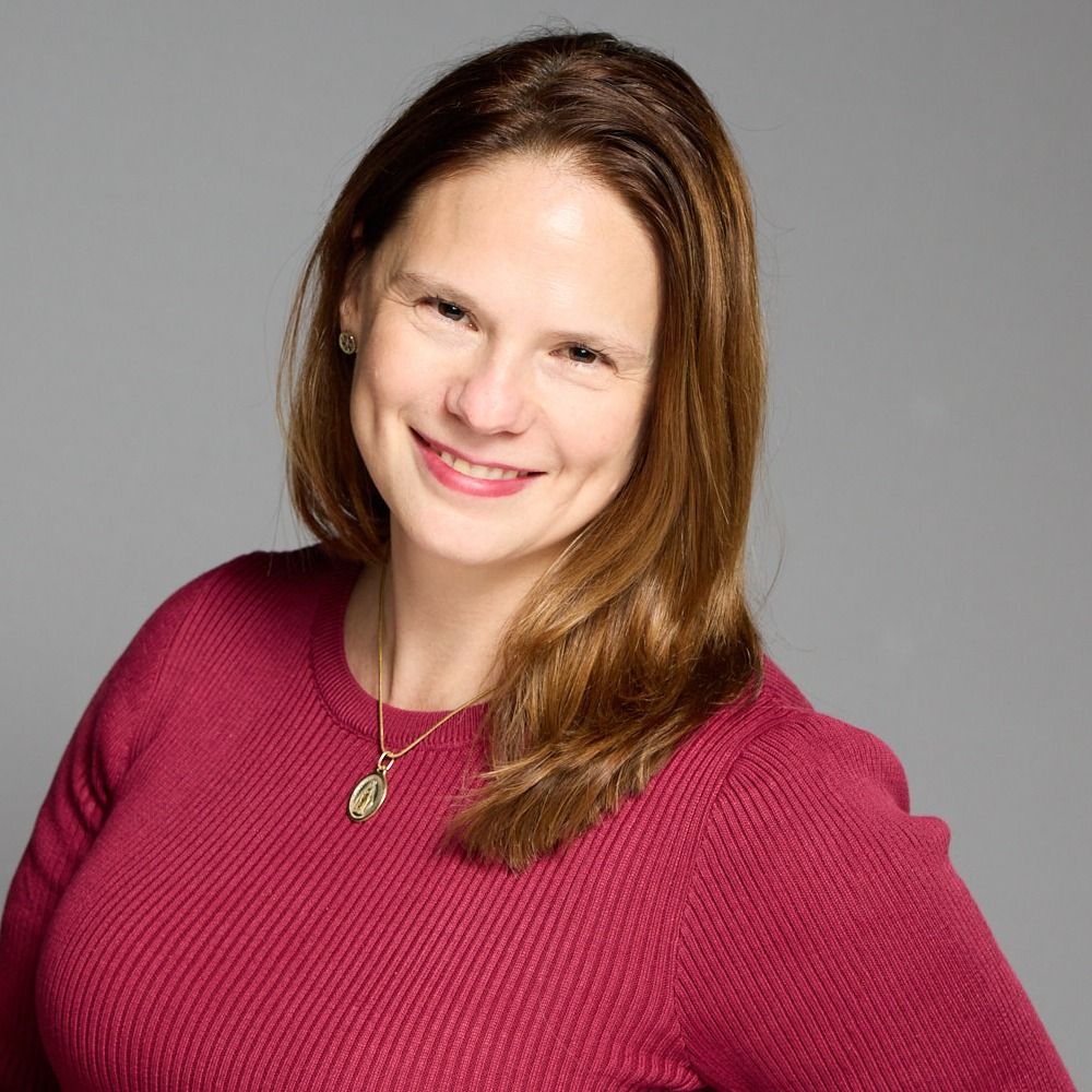 A woman wearing a red sweater and a necklace is smiling for the camera.