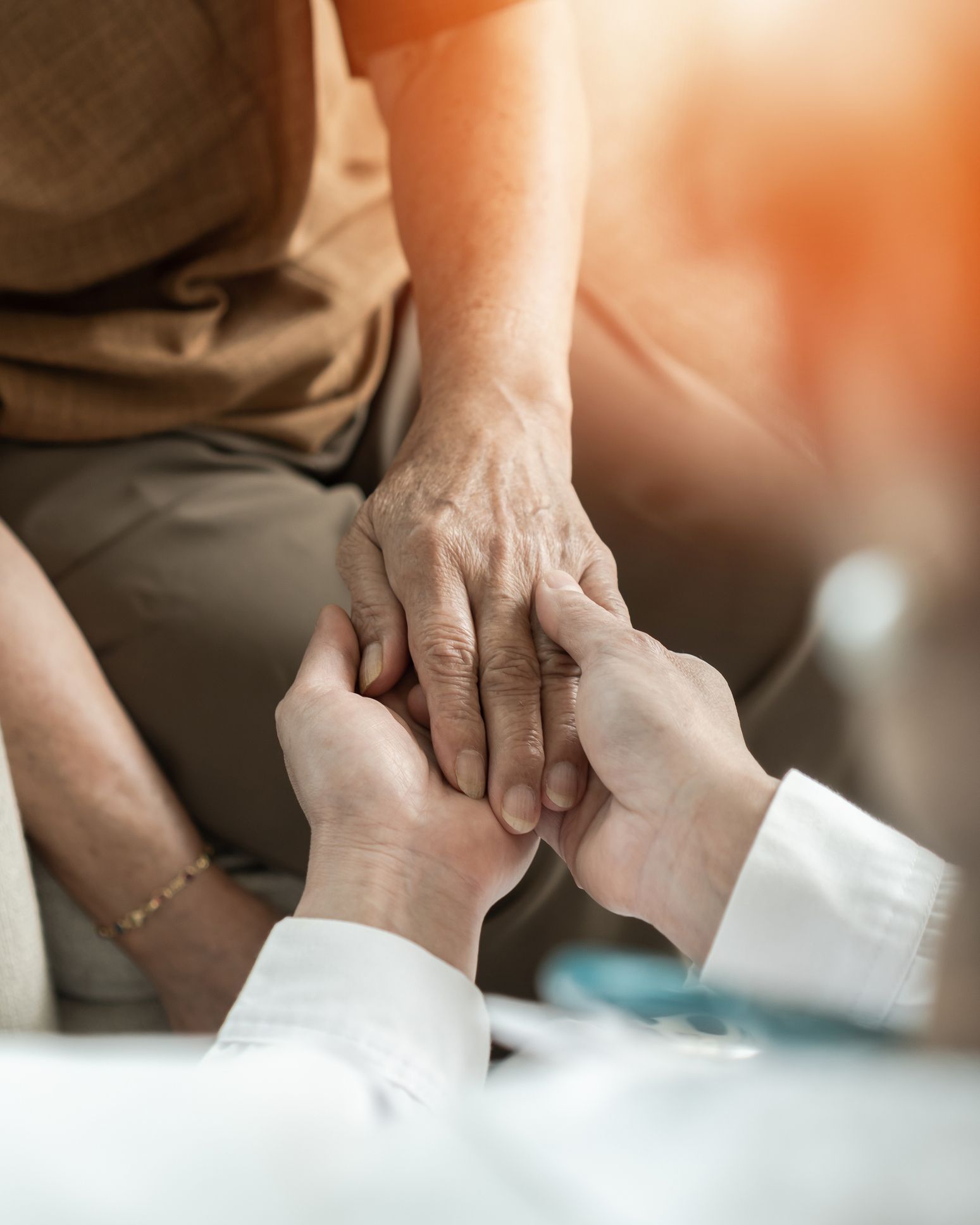 A doctor is holding a patient 's hand in a hospital bed.