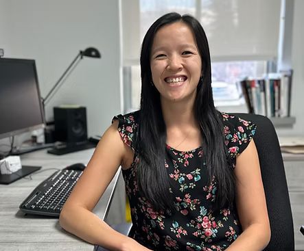 Une femme est assise à un bureau devant un ordinateur et sourit.
