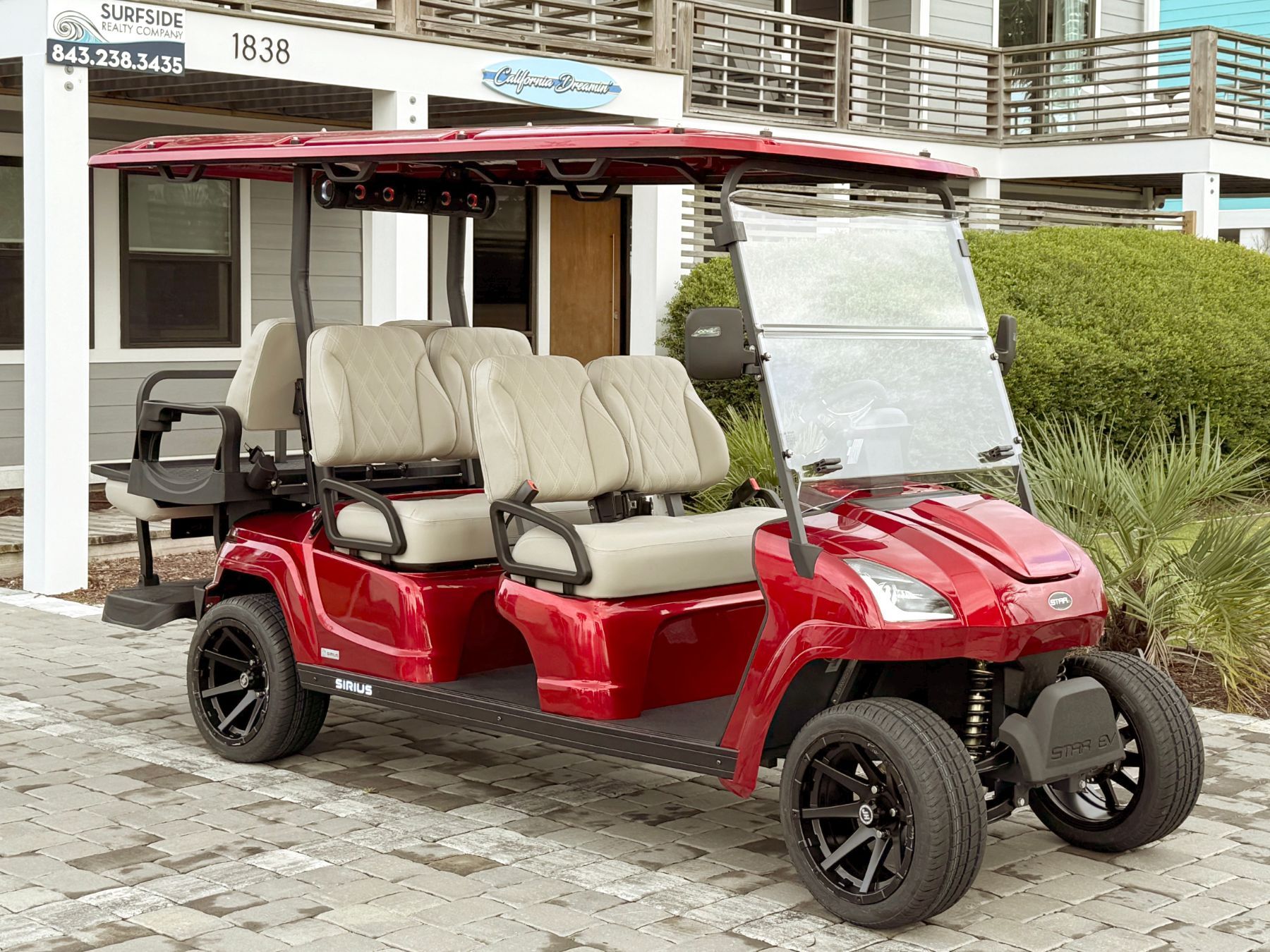Red golf cart with black wheels parked near a light blue building.