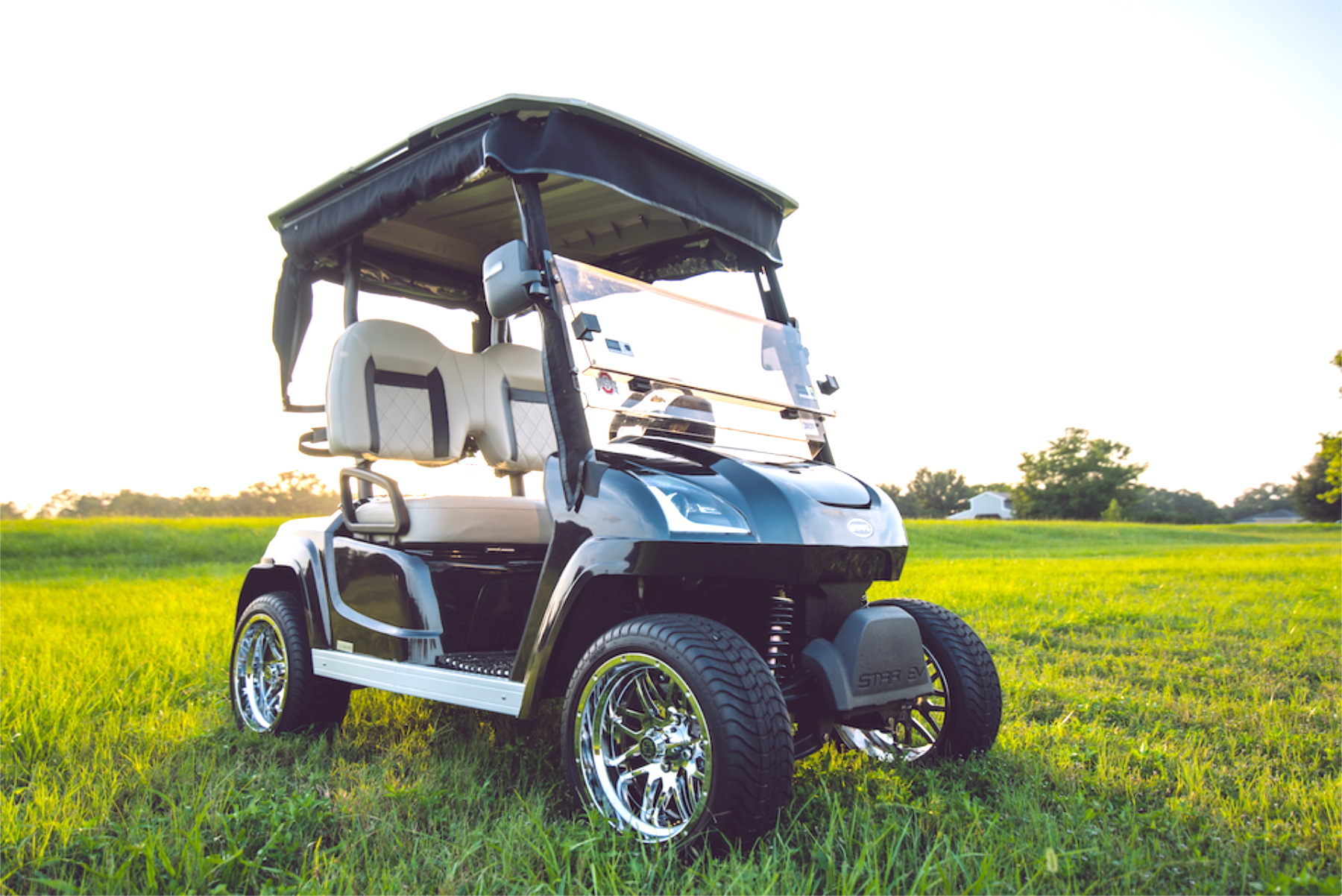 Black golf cart with beige seats and chrome wheels on a grassy field.