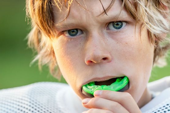 Boy wearing a green mouthguard, looking determined, set against a blurred green background.