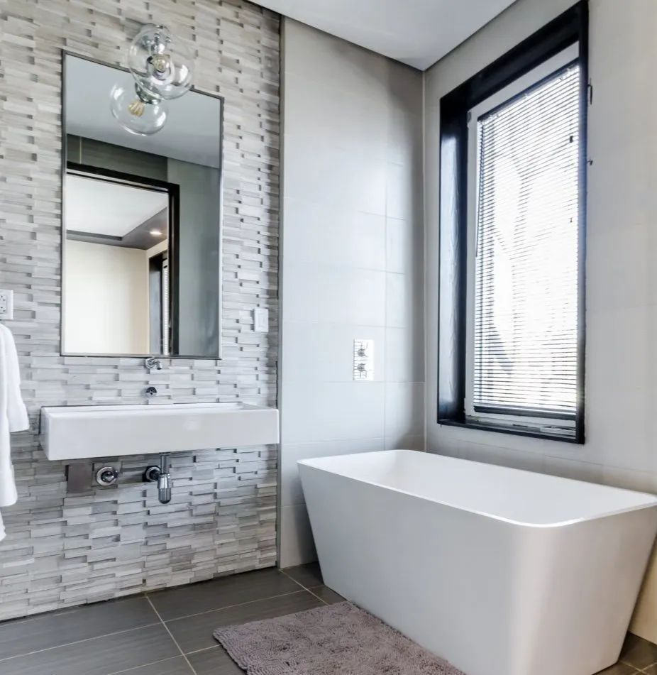 A bathroom with a tub , sink , mirror and window