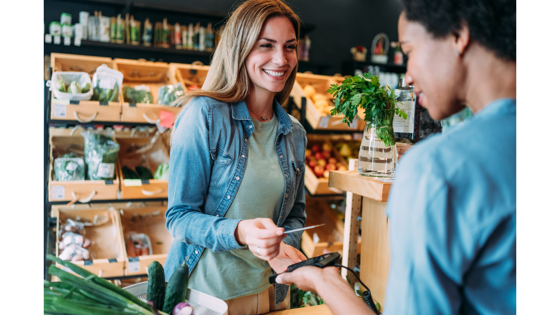 A woman is giving a credit card to a man in a grocery store.