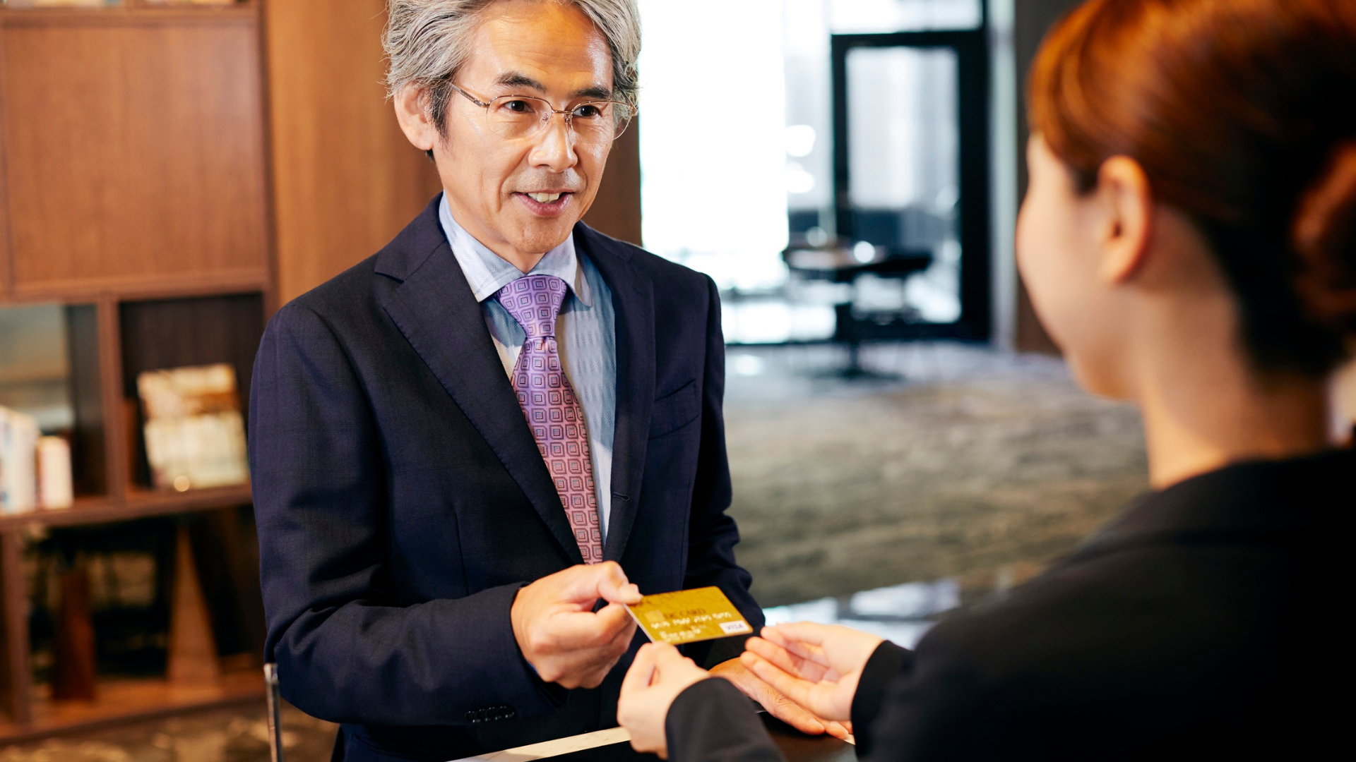A man in a suit and tie is giving a credit card to a woman.