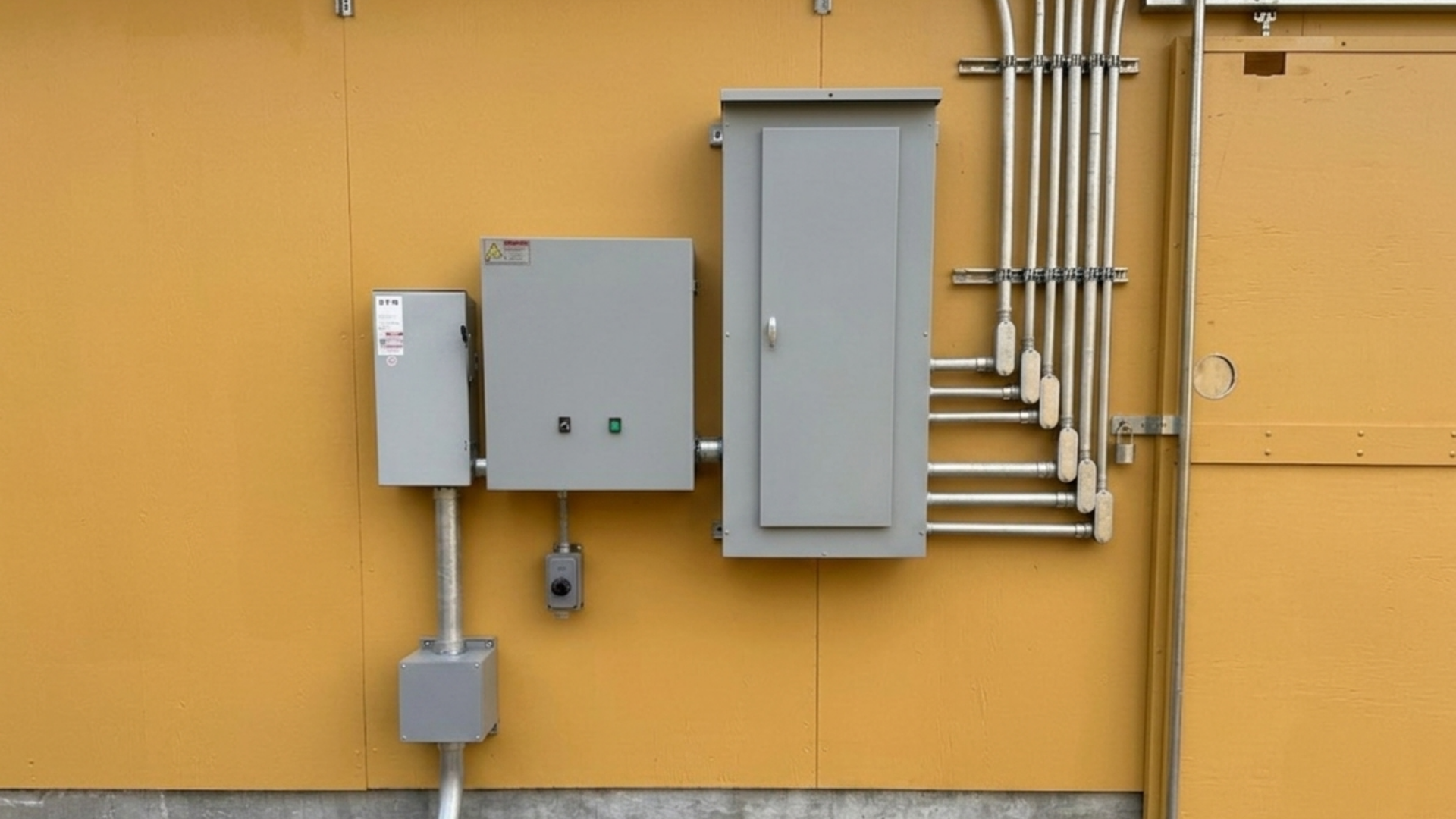 Gray utility boxes and conduit mounted on a yellow exterior wall
