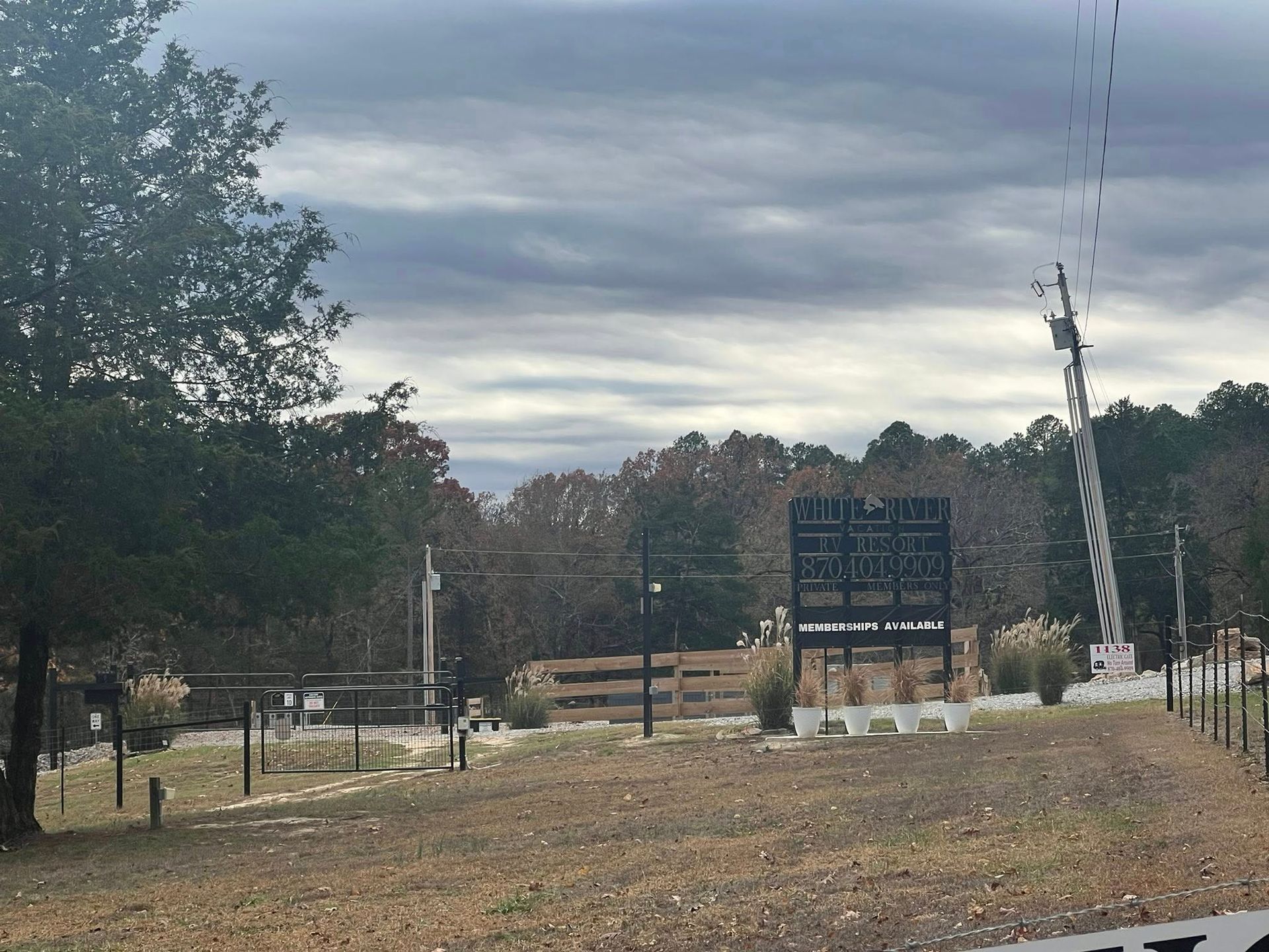 A scoreboard sits in a grassy field with a cloudy sky backdrop and trees.