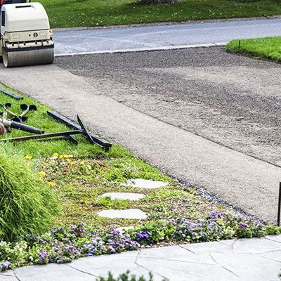 a man is using a roller to spread asphalt on a driveway .