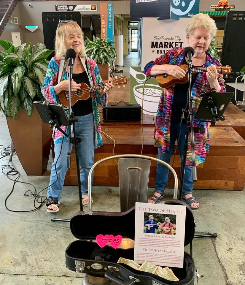 two women singing and playing ukuleles in a market square