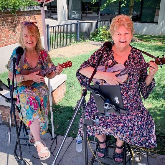 Two women are playing ukuleles in front of microphones.