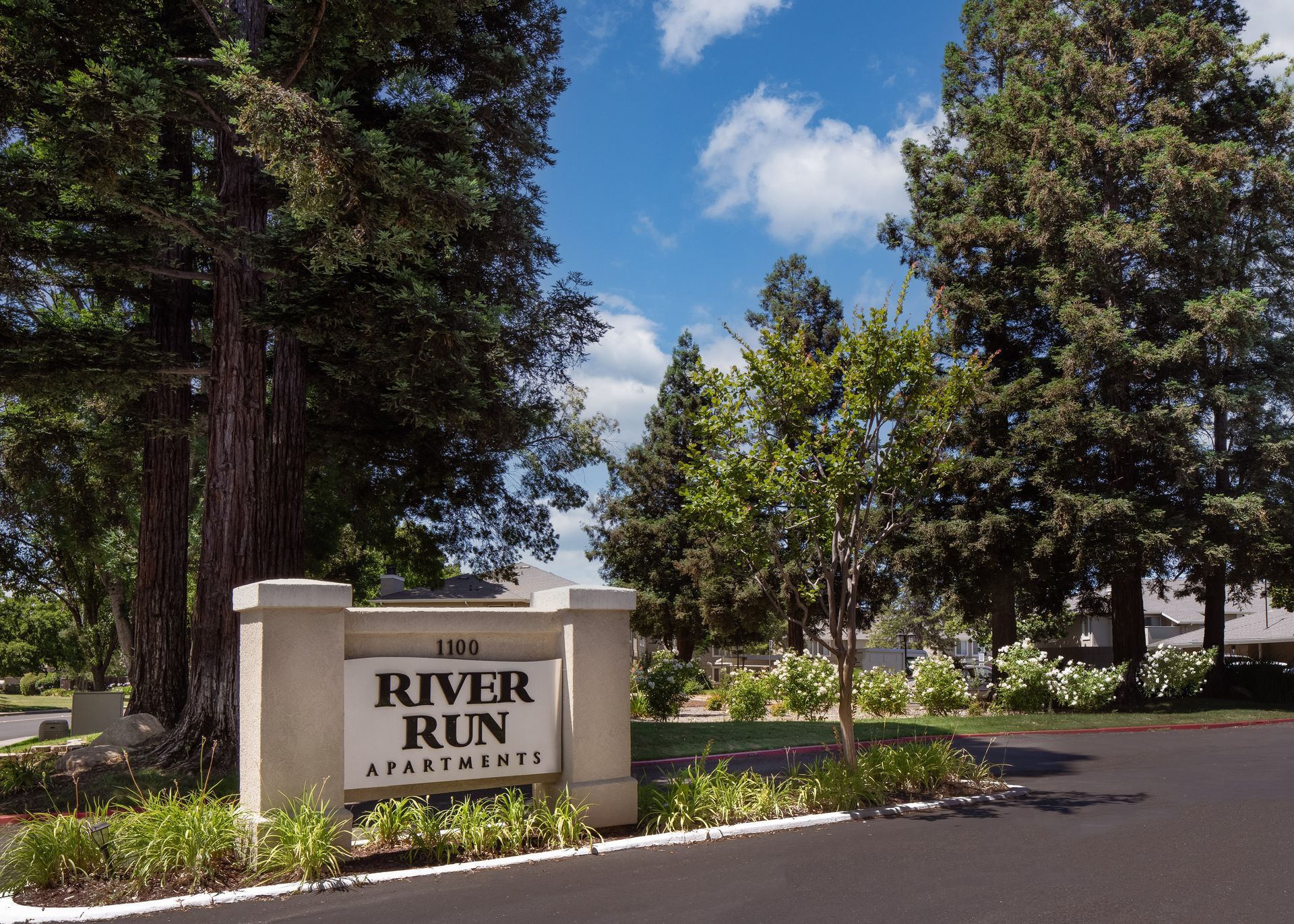 Sign for River Run Apartments under trees on a sunny day.