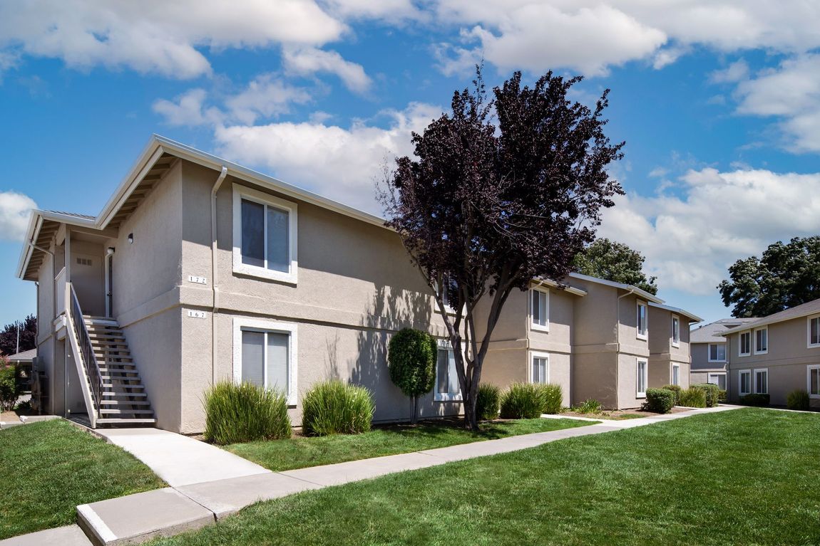 Apartment building with beige exterior, green lawn, blue sky.
