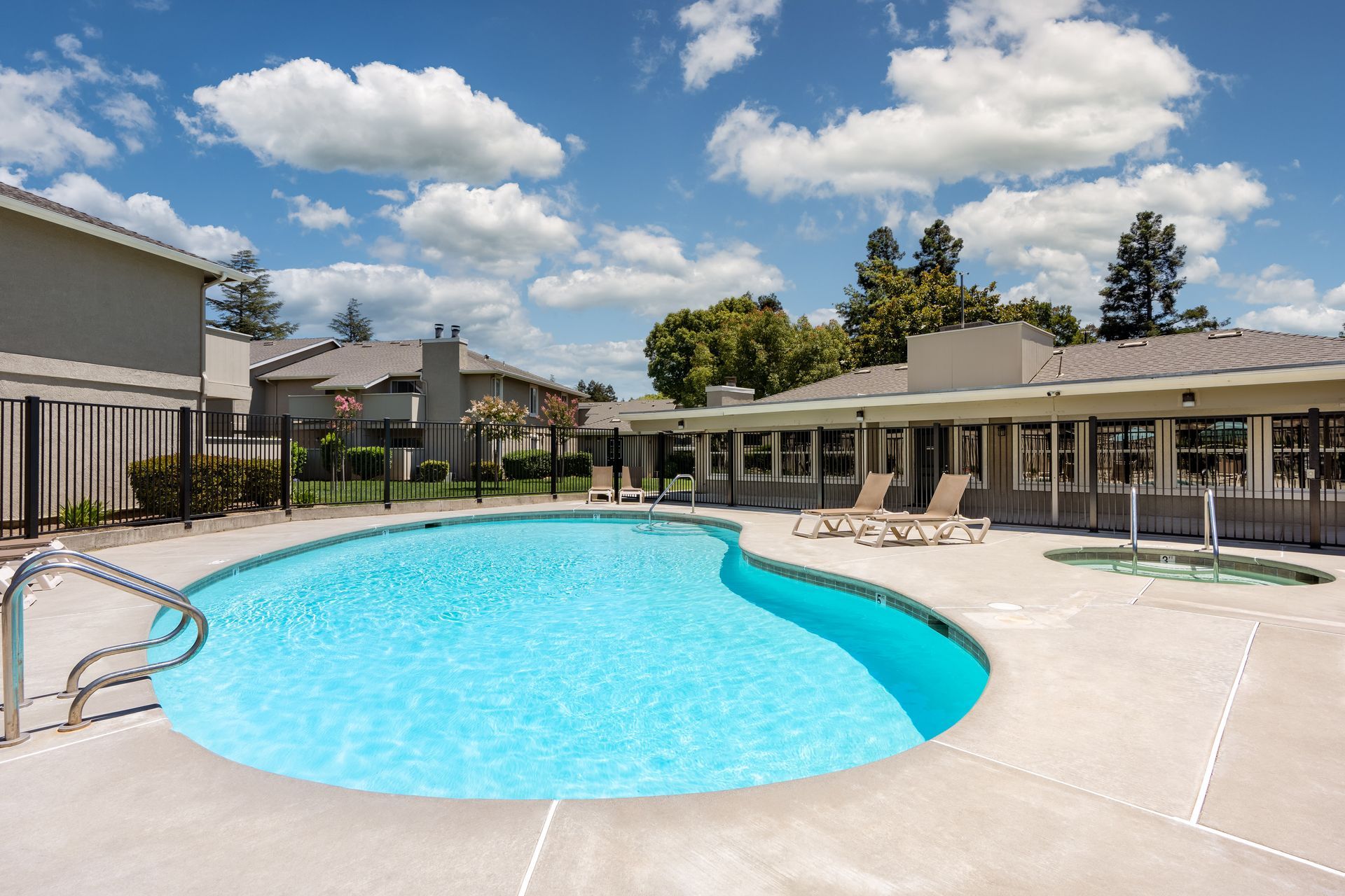 Swimming pool with lounge chairs and two-story apartment buildings on a sunny day.