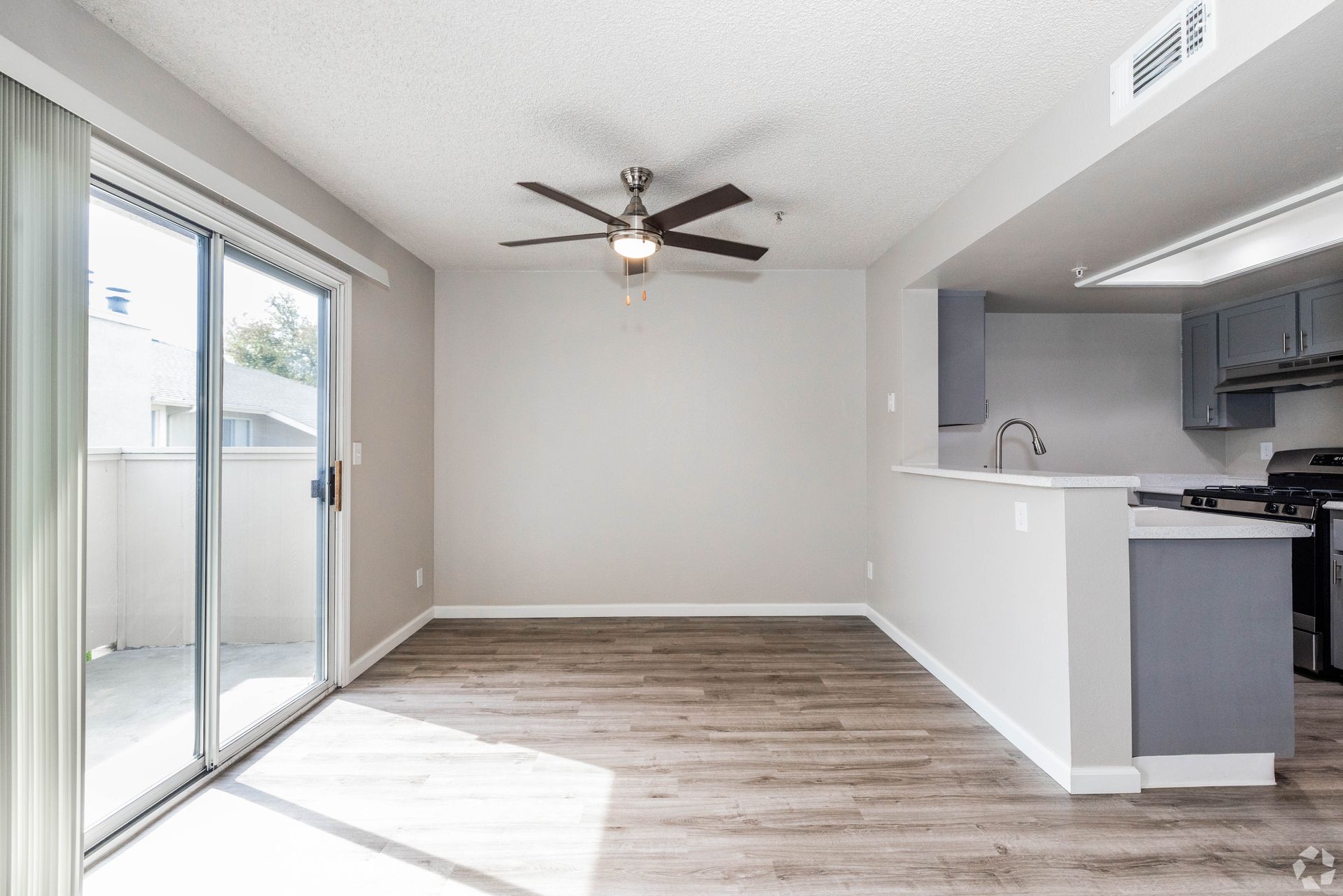 Bright, empty living space with a sliding door to a balcony and an open kitchen with a breakfast bar.