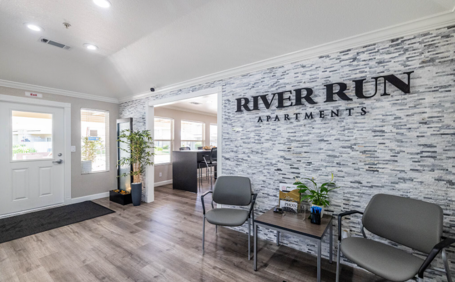 River Run Apartments reception area: Grey chairs, white brick wall, logo, wooden floor, bright.