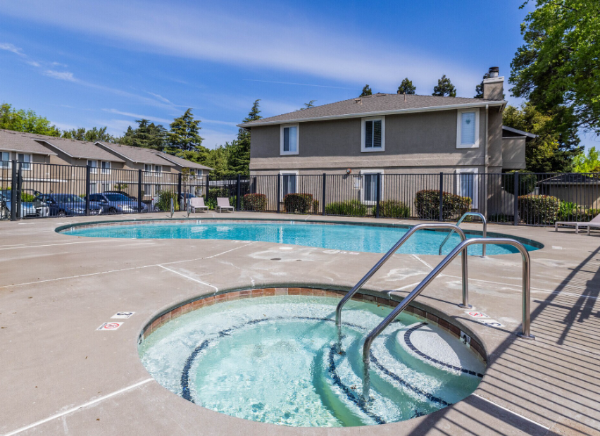 Pool and jacuzzi at apartment complex on sunny day.