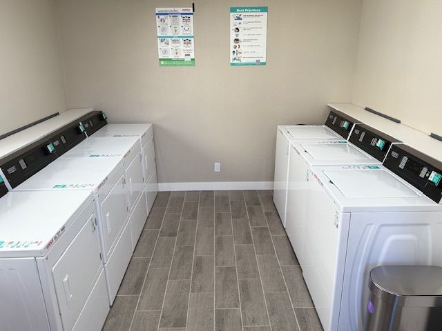 Laundry room with two rows of white washers and dryers, tiled floor, and informational posters.
