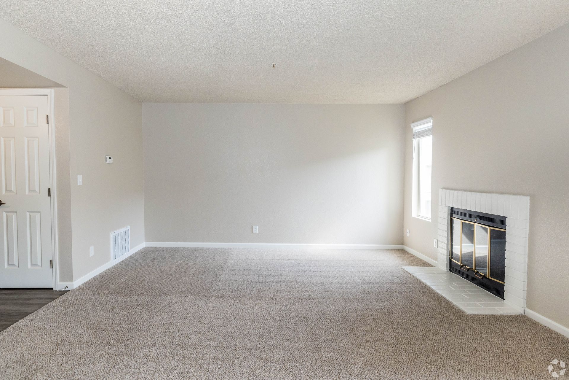 Empty living room with beige walls, carpet, fireplace, and a door.