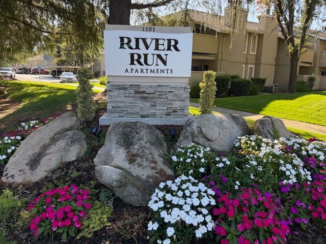 Apartment building with carports under a blue sky with fluffy clouds. Cars are parked in designated spots.