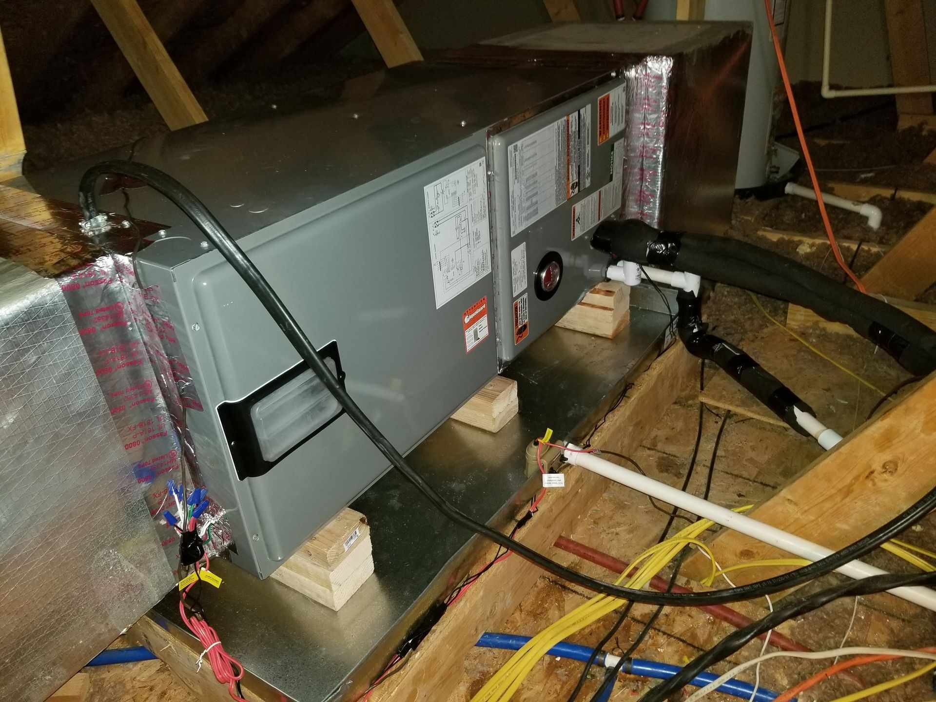 An air conditioner is sitting in the attic surrounded by wires.