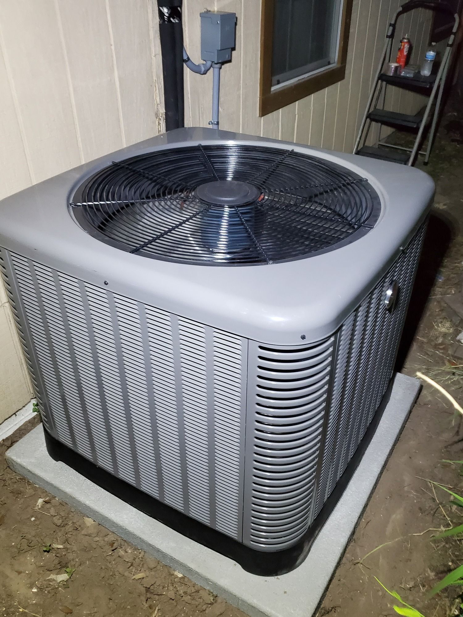 A large gray air conditioner is sitting on top of a concrete platform.