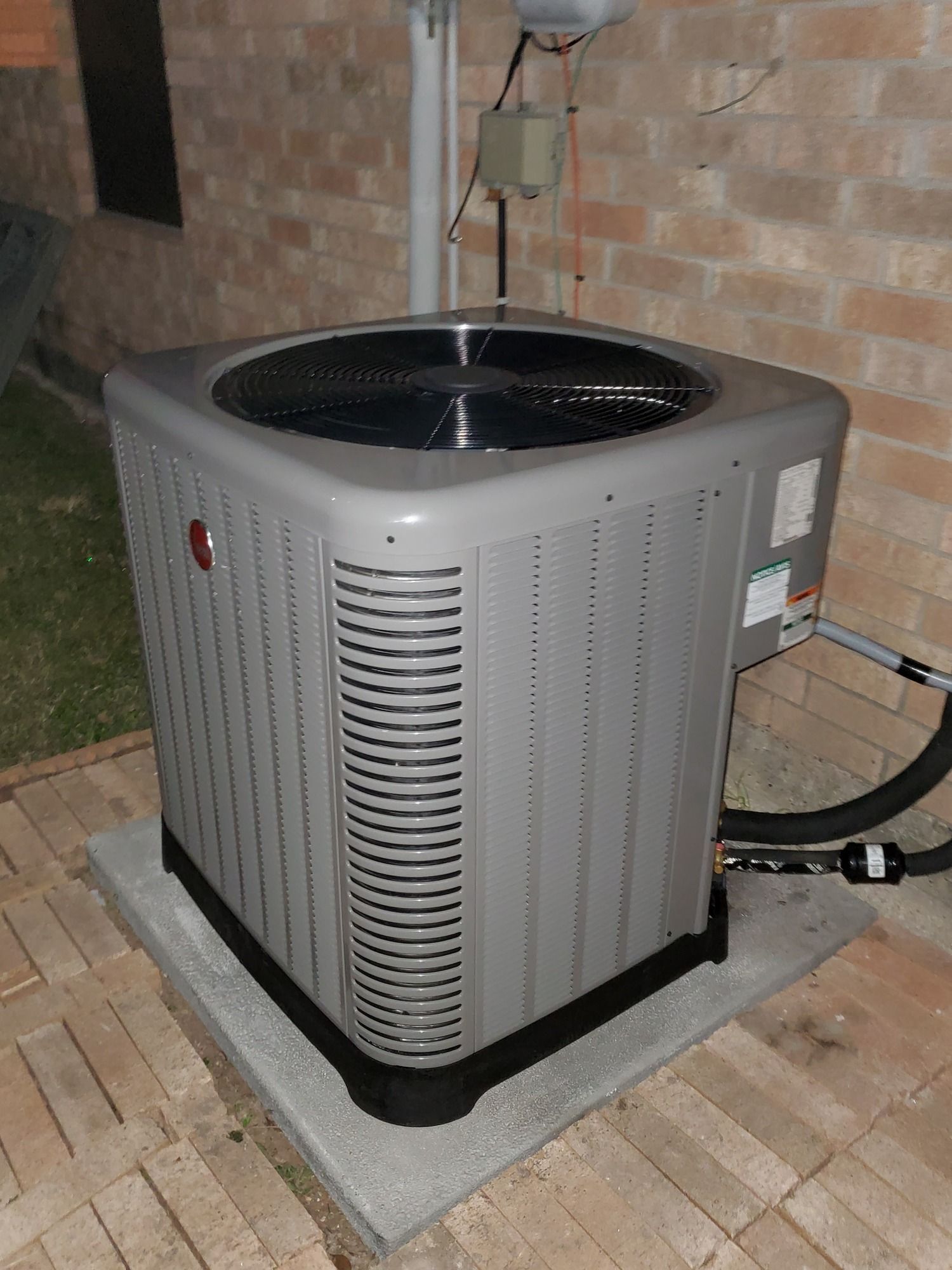 A gray air conditioner is sitting on a tiled floor next to a brick wall.