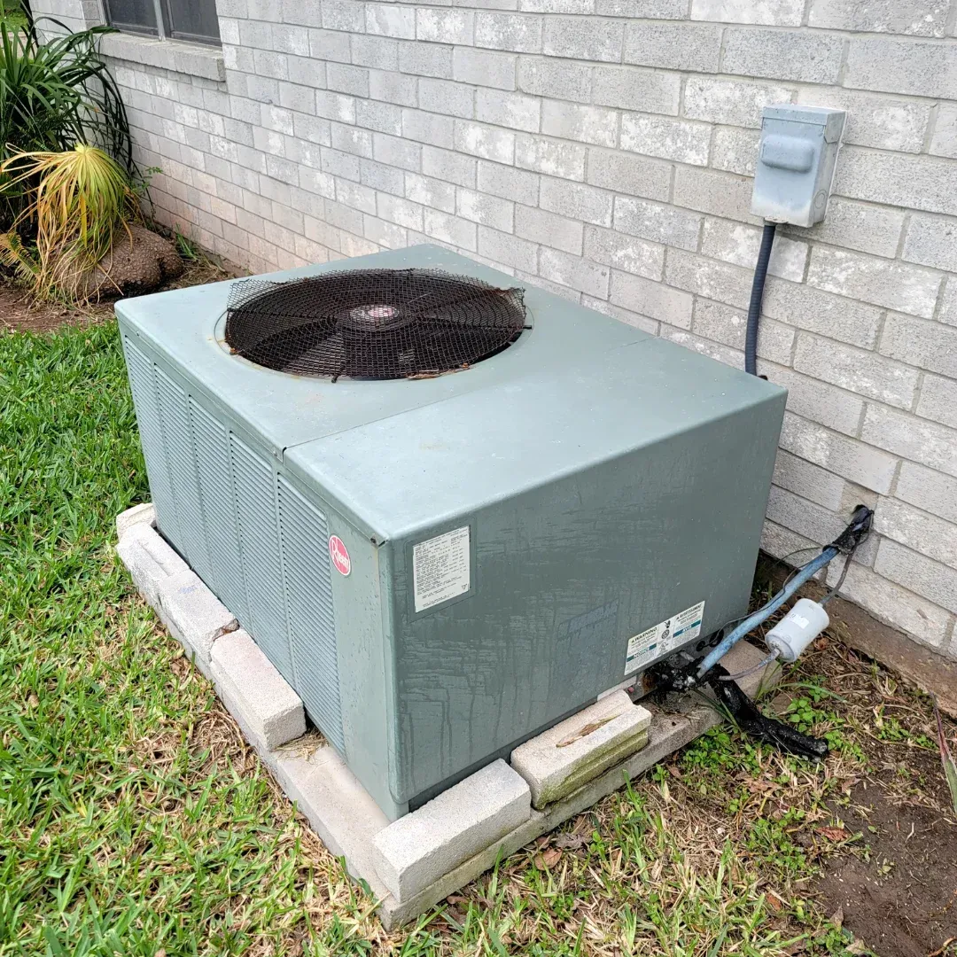 A green air conditioner is sitting on top of a brick wall.