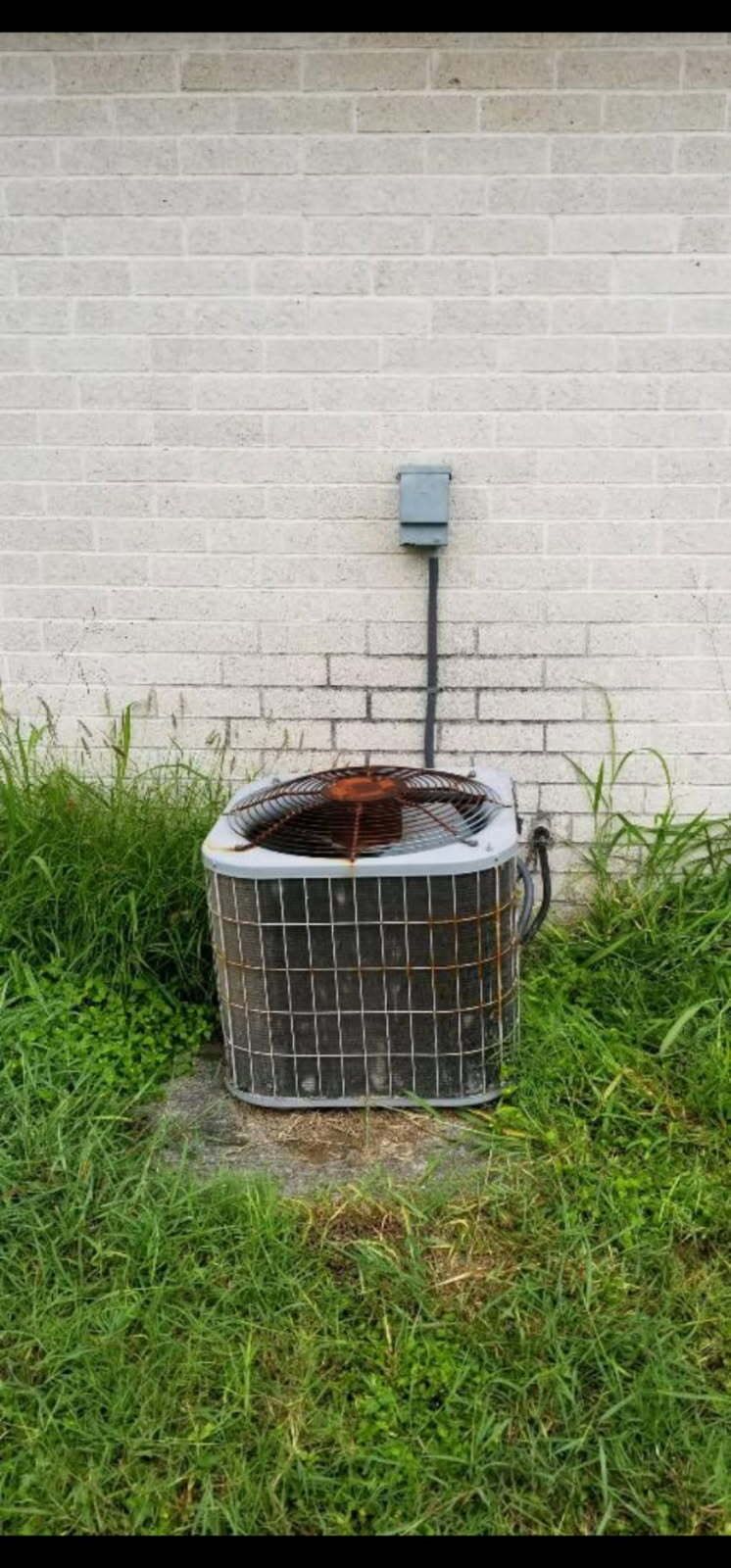 Two air conditioners are sitting outside of a house.