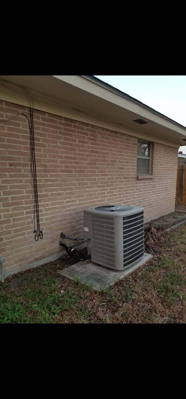Two air conditioners are sitting outside of a house.