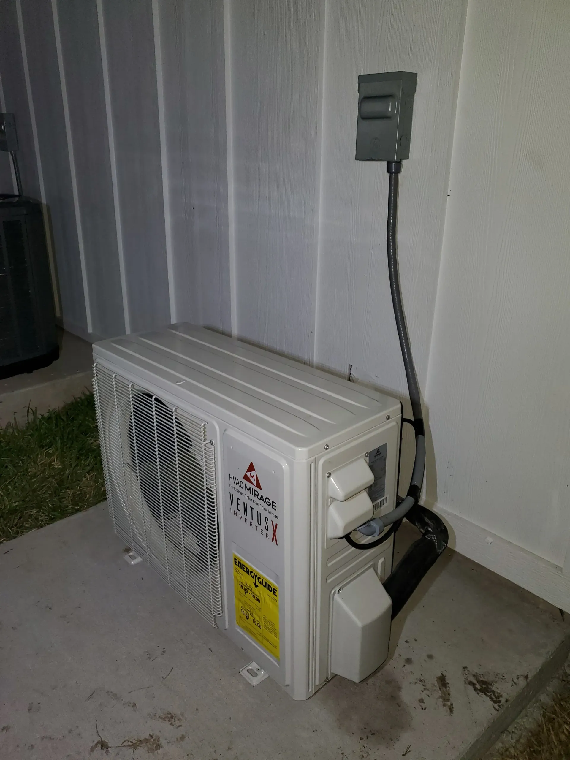 A white air conditioner is sitting on the side of a building next to a wall.